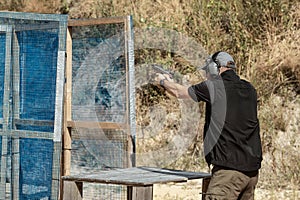 Man in tactical clothes shooting from a pistol, reloading the gun and aiming at the target in the open-door Shooting range.