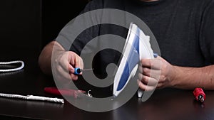 A man takes apart an iron with a screwdriver. Repairing a burnt iron at home. Tools for repair are on the table nearby