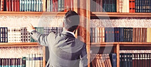 Man takes book from bookcase. Student stands in library and choose book. Guy in smart suit reads near bookcase. Study