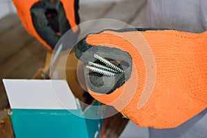 a man takes fasteners out of the box and twists them in his hands; hands in orange gloves