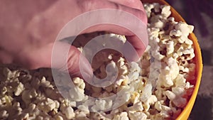 A man takes fresh hot popcorn from a bowl. A male hand picks popcorn from a bucket.