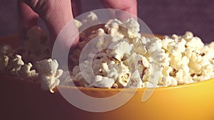 A man takes fresh hot popcorn from a bowl. A male hand picks popcorn from a bucket. A man grabs popcorn from a bucket while watch