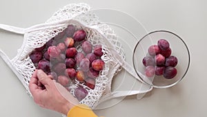 Man takes fresh ripe Plums out from reusable grocery bag with fruits