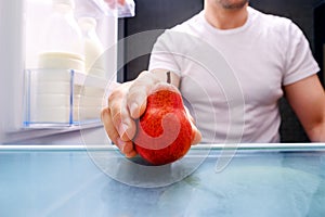 Man takes out red pear from refrigerator inside look