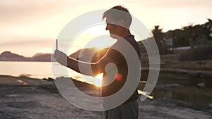 A man takes a photo of the sea at sunset on a mobile phone.