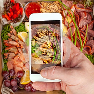 A man takes pictures of food on his phone. Shrimp, snack, fruit, meat, vegetables. A picture of food on your phone screen