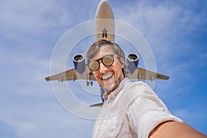 A man takes a selfie against the sky and a flying plane