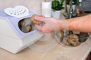 man takes spud from vegetable container. box storing potato, onion, carrot. Container with ventilation, without light