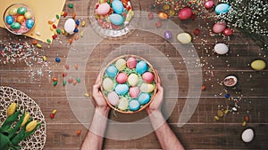 Man taking basket with easter egg from the table decorated with easter eggs. Top view