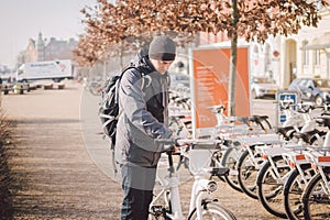 Man taking bike in bike sharing. Man take city bicycle vacation at the parking. Public electric bikes for rent parked in