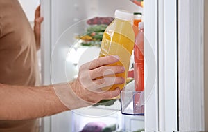 Man taking bottle with juice out of refrigerator in kitchen