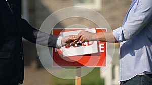 Man taking house keys and shaking hand of estate agent, successful deal, sale