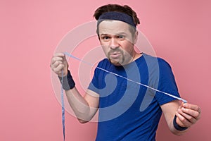 Man taking measurements of his body by centimeter line. He looks amazed as does not see results of his traning