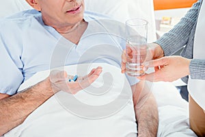 Man taking medicines and woman holding glass of water