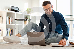 Man Taking Notes Using Laptop Sitting On Floor At Home