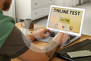 Man taking online test on laptop at desk indoors, closeup