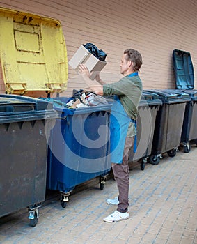 Man taking out big paper box on trash into garbage container.