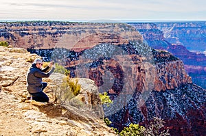Man taking photo on ledge of Grand Canyon South Rim Arizona