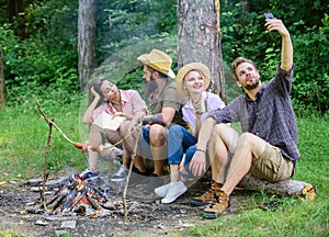 Man taking photo near bonfire nature background. Tourists sit log near bonfire taking selfie photo smartphone. Friends