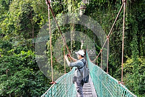 Man taking photo with smart phone at suspension bridge in tree top canopy walkway in Danum rain forest Lahad datu