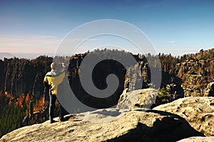 Man is taking photos by smartphone on peak in rock empires park and watching over autumn misty valley.