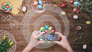 Man taking picture of basket with easter eggs on table decorated with easter eggs. Top view