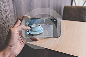 Man taking a picture of a coffee cup with her smart phone while sitting at a coffee shop.