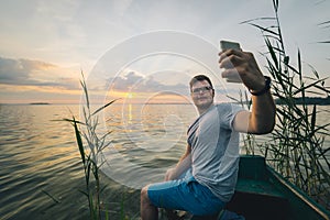 Man taking picture on his phone of sunrise while sitting in old boat