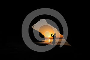Man taking picture of sunset, beautiful red sky In front of a cave on the beach