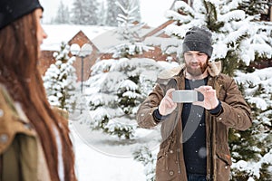 Man taking pictures of his girlfriend with smartphone in winter