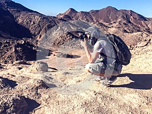 Man taking pictures on the top of mountain in the desert. Travel and hobby concept