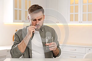 Man taking pill against migraine in kitchen, space for text