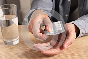 Man taking pill out from blister pack at wooden table, closeup