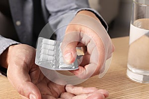 Man taking pill out from blister pack at wooden table, closeup