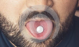 Man taking pill, tablet of drugs or medicine on tongue with open mouth. Painkiller treatment or party narcotic