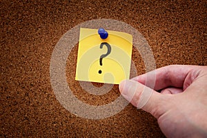 A man taking a pinned paper note with a question mark from a cork board