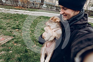 man taking selfie with adorable brown puppy with amazing blue eyes on background of autumn park. space for text. faithful friend