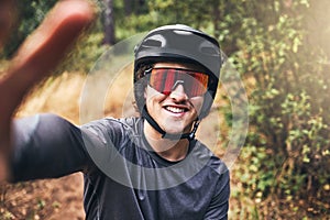 Man taking a selfie while cycling on a nature trail, wearing a helmet and sunglasses. Portrait of a cyclist on bicycle