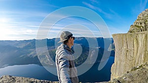 A man taking a selfie and hiking along a fjord in Norway. In fornt of him is the famous Preikestolen mountain.