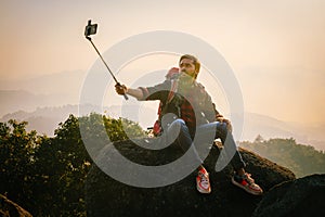 man is taking a selfie with his cell phone while sitting on a rock