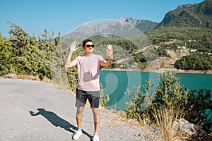 Man taking selfie on mobile phone of mountains lake background. Traveler male having video chat on cellphone on the blue