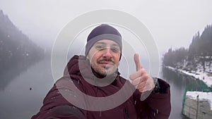 Man taking selfie and showing thumb up at Ritsa lake in Abkhazia in winter.