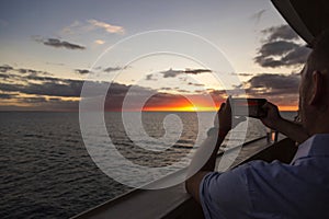 Man taking a smartphone photo of a beautiful sunset while enjoying an evening on a luxury cruise ship