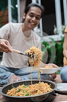 man taking a spoon full of noodle during picnic with friend