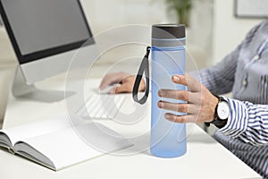 Man taking transparent plastic bottle of water while working on computer in office, closeup