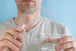 Man taking white pill of statin medicine to treat high cholesterol with glass of water on blue background