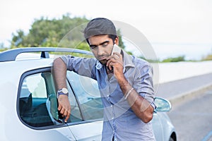 Man talking on a cell phone leaning on the door of his car