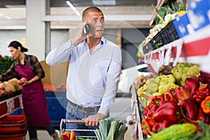 Man talking on cellphone while buying vegetables and fruits at market