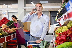 Man talking on cellphone while buying vegetables and fruits at market