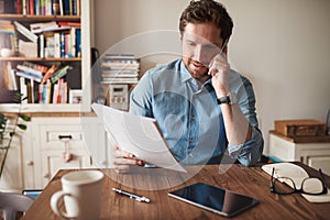 Man talking on a cellphone while reading paperwork at home